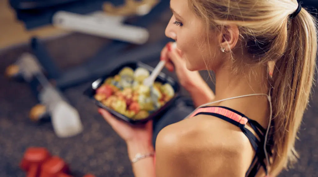 Athlete in workout gear eating a balanced diet meal with fresh vegetables and protein from a black container