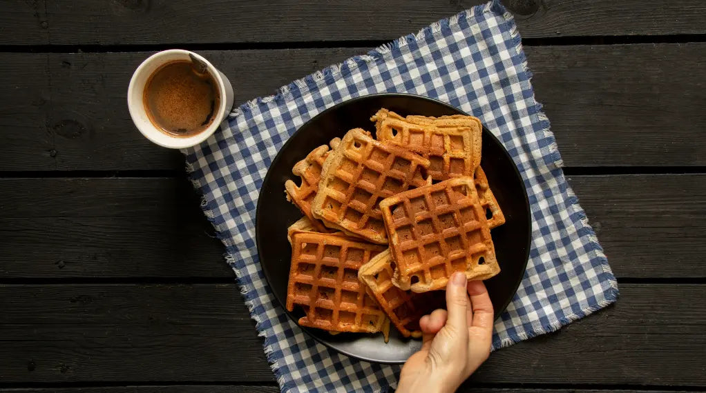 Breakfast dish of golden waffles served with coffee on checkered napkin