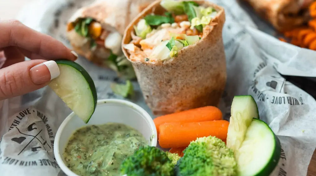 A veggie-packed wrap served with fresh carrots, broccoli, cucumber, and herb dip — a colorful and satisfying light bite.