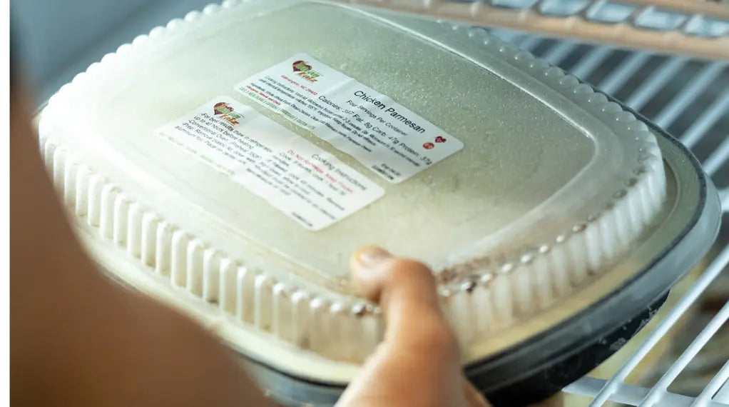 A hand placing a labeled Clean Eatz Chicken Parmesan container on a freezer shelf — simple meal preservation and management at home.