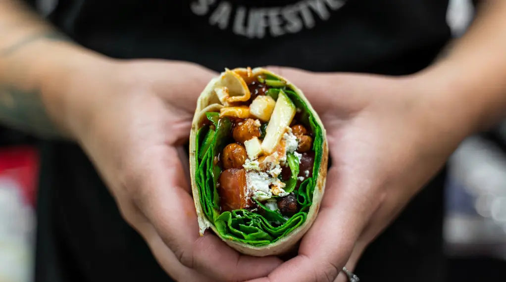 A Clean Eatz staff member holding a cross-section wrap filled with chickpeas, greens, and BBQ sauce — nourishing and light in every bite.