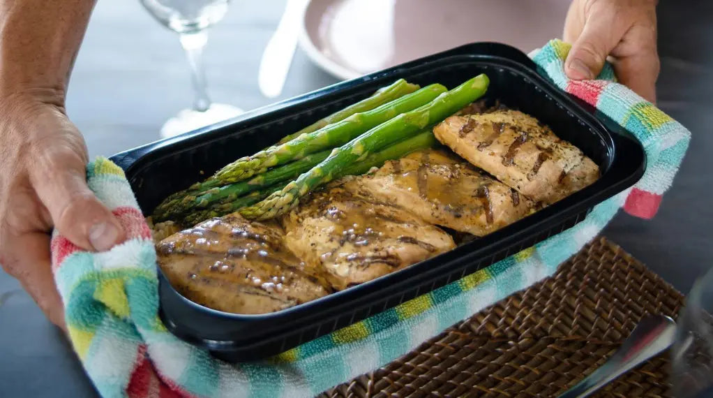 Hands holding a nutrient-rich diet meal with grilled salmon fillets and roasted asparagus in a black container