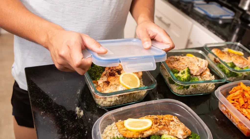 Person holding portion-controlled meal container with salmon, broccoli, and grains