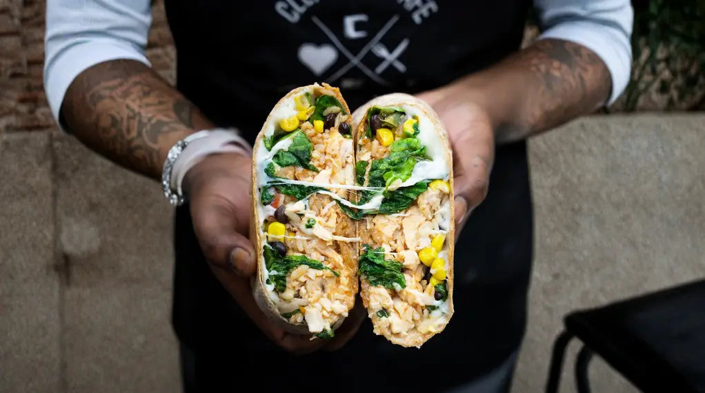 Hands holding protein-packed wrap filled with rice, greens, and corn