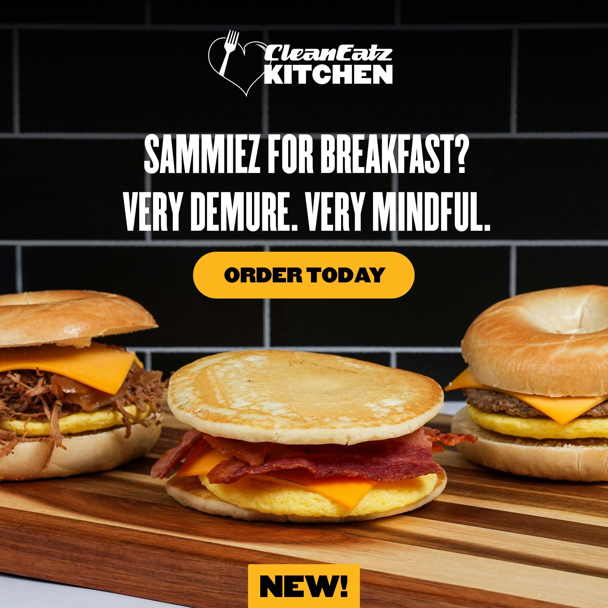  A promotional Clean Eatz Kitchen image showcasing three Breakfast Sammiez sandwiches on a wooden board. The sandwiches include a pulled meat and cheese bagel, a bacon, egg, and cheese pancake sandwich, and a sausage, egg, and cheese bagel. The ad copy reads: 