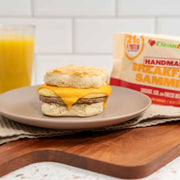Breakfast sandwich on a plate with a side of orange juice and a package of Clean Falz breakfast sammies.
