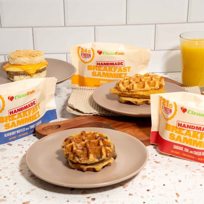 Handmade breakfast sandwiches and waffles on plates with packaging in the background.