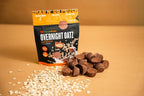 Clean Eatz Overnight Oatz ‘Peanut Butter Cup’ grab-n’-go pouch on a tan background with rolled oats and mini peanut butter cups scattered in front.