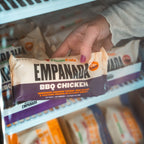 Hand holding a package of Clean Eatz Empanada BBQ Chicken in front of a store shelf.