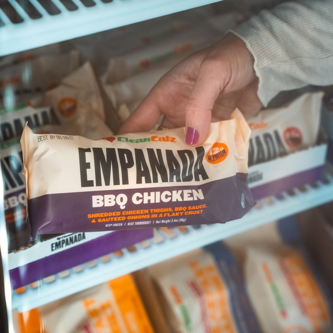 Hand holding a package of Clean Eatz Empanada BBQ Chicken in front of a store shelf.