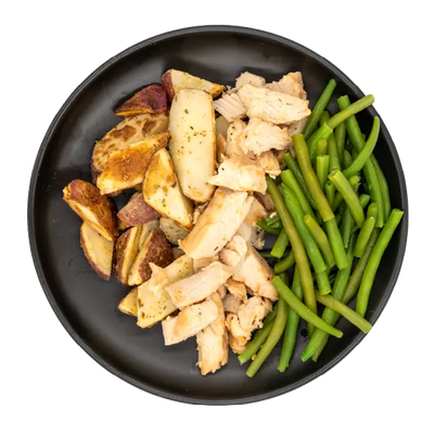 Diced chicken with green beans and roasted red potatoes on a black plate.