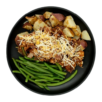 BBQ chicken topped with shredded cheese and bacon, served with green beans and roasted red potatoes on a black plate.