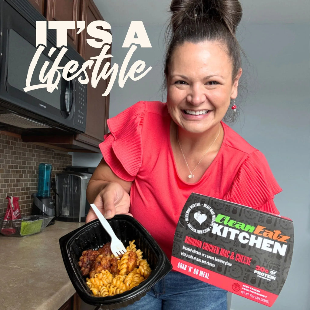 Woman holding a Clean Eatz Kitchen Bourbon Chicken Mac & Cheese grab-and-go meal with 30g protein in her kitchen