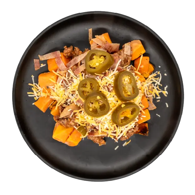 Chopped brisket over roasted sweet potatoes with shredded cheese, bacon, and sliced jalapeños on a black plate.