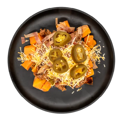Chopped brisket over roasted sweet potatoes with shredded cheese, bacon, and sliced jalapeños on a black plate.
