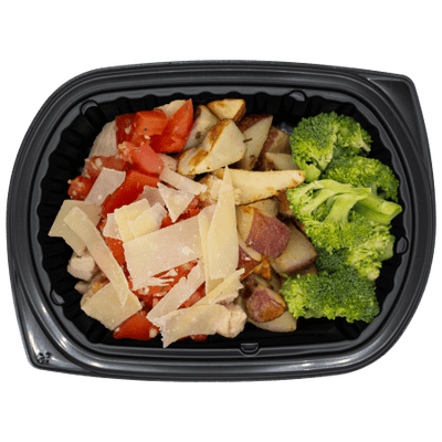 Chicken topped with diced tomatoes and parmesan over roasted red potatoes with a side of broccoli in a black meal tray.