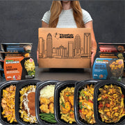 Person holding a Clean Eatz Kitchen box with various food packages displayed in front.
