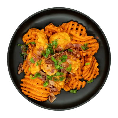 Chicken over sweet potato waffle fries topped with queso, bacon, and green onions on a black plate.