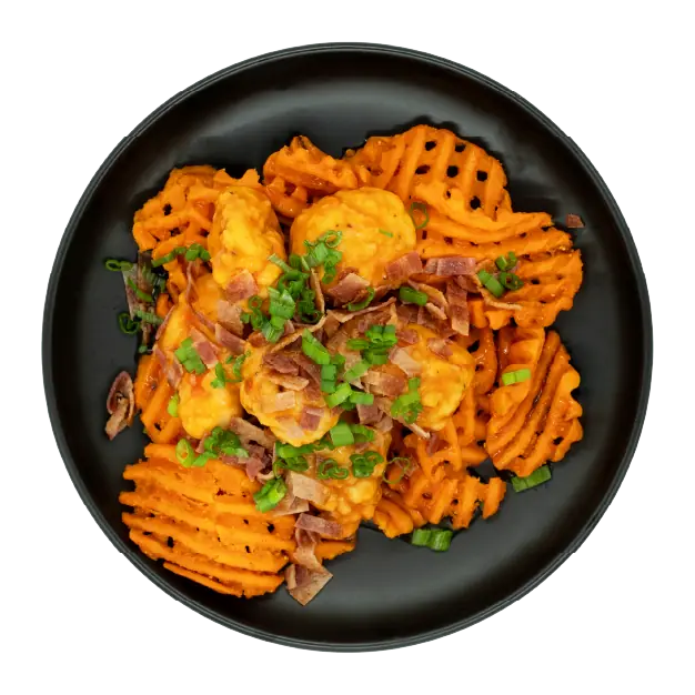Chicken over sweet potato waffle fries topped with queso, bacon, and green onions on a black plate.