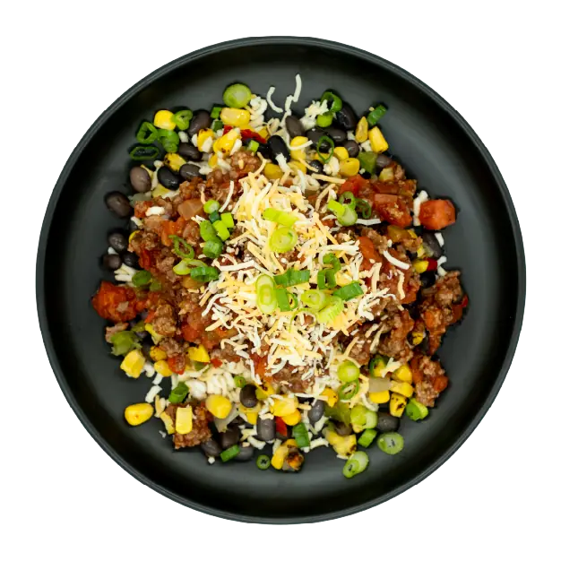 Chicken taco bowl with corn, black beans, salsa, shredded cheese, and green onions over rice on a black plate.