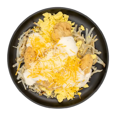 Scrambled eggs with hash browns, chicken bites, gravy, and shredded cheese on a black plate.