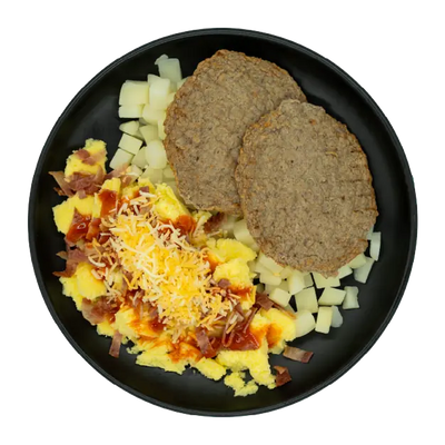 Turkey sausage patties with scrambled eggs, diced potatoes, shredded cheese, bacon, and gravy on a black plate.