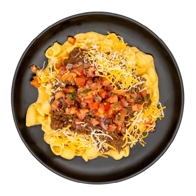 Shredded brisket over mac and cheese topped with diced tomatoes, pico de gallo, and shredded cheese on a black plate.
