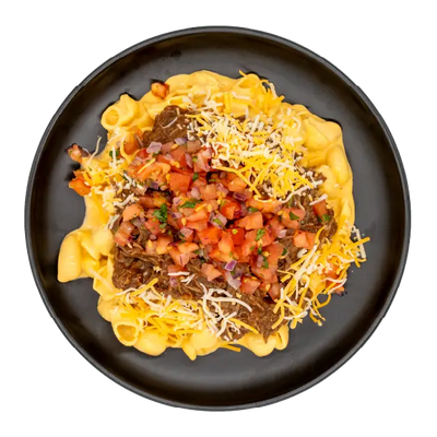 Shredded brisket over mac and cheese topped with diced tomatoes, pico de gallo, and shredded cheese on a black plate.
