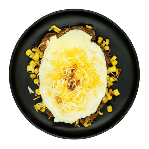 Cowboy shepherd’s pie with mashed potatoes, corn, shredded cheese, and crispy onion straws on a black plate.
