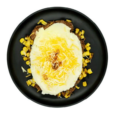 Cowboy shepherd’s pie with mashed potatoes, corn, shredded cheese, and crispy onion straws on a black plate.