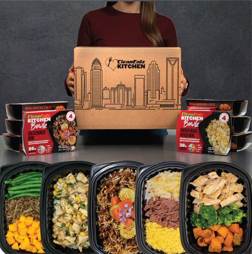 Person holding a Clean Eatz Kitchen box with various prepared meals displayed in front.