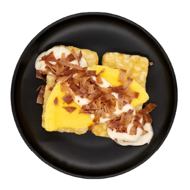 Egg omelette with bacon over hash browns in a light gravy on a black plate.