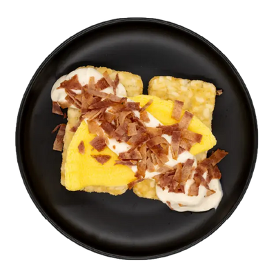 Egg omelette with bacon over hash browns in a light gravy on a black plate.