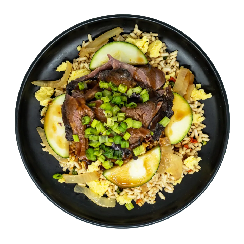 Prime rib with zucchini, caramelized onions, scrambled eggs, and green onions over hibachi-style fried rice on a black plate.