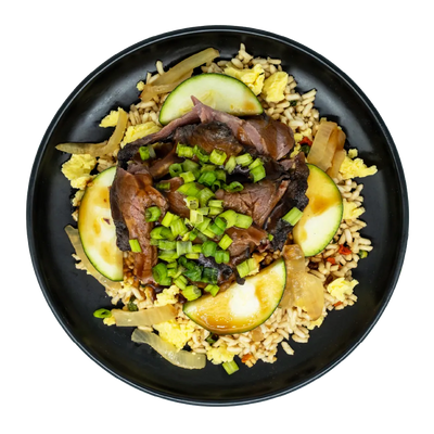 Prime rib with zucchini, caramelized onions, scrambled eggs, and green onions over hibachi-style fried rice on a black plate.