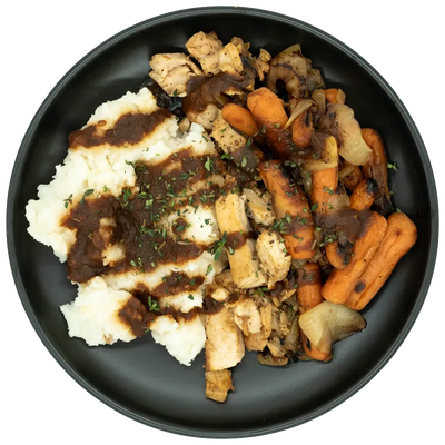 Seasoned chicken with mashed potatoes, roasted carrots, mushrooms, and onions topped with brown gravy on a black plate.