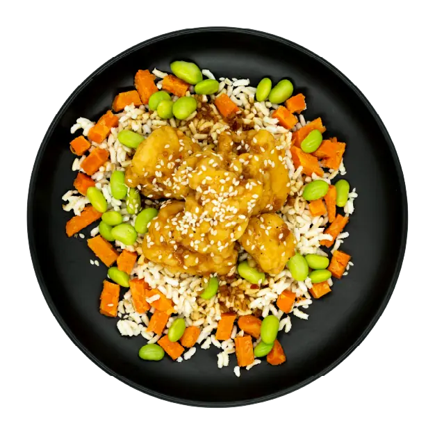 Korean BBQ chicken bites over rice with edamame and carrots on a black plate.