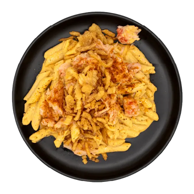 Lobster mac and cheese topped with crispy onion straws on a black plate.