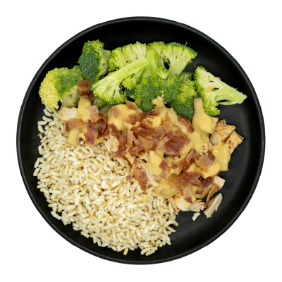 Chicken topped with maple sauce and crispy bacon, served with broccoli and brown rice on a black plate.