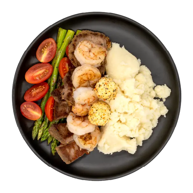 Steak and shrimp with asparagus, tomatoes, mashed potatoes, and seasoned butter on a black plate.