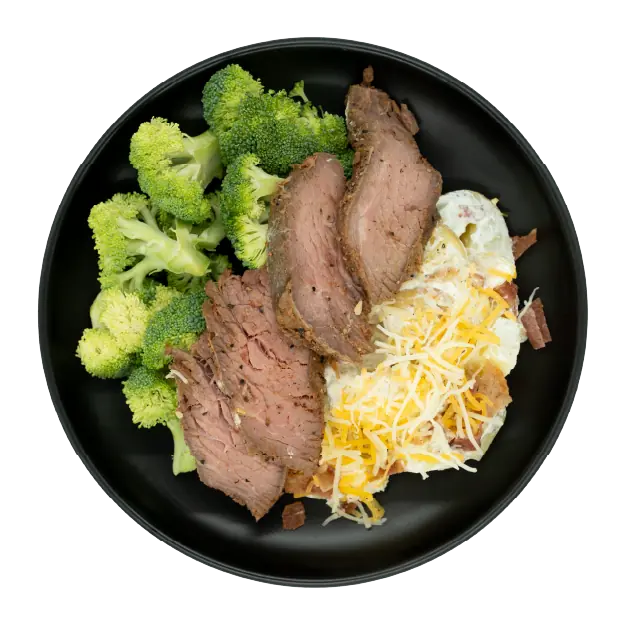 Tri-tip steak with broccoli and loaded mashed potatoes topped with shredded cheese and bacon on a black plate.
