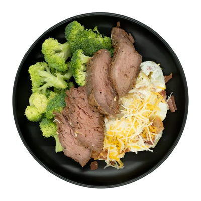 Tri-tip steak with broccoli and loaded mashed potatoes topped with shredded cheese and bacon on a black plate.