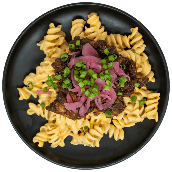BBQ turkey burnt ends over creamy mac and cheese topped with pickled red onions and green onions on a black plate.