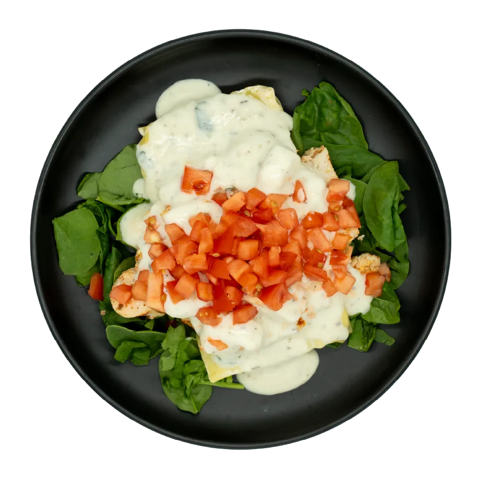 Chicken lasagna with creamy white sauce, diced tomatoes, and spinach on a black plate.