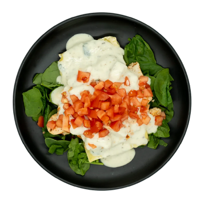 Chicken lasagna with creamy white sauce, diced tomatoes, and spinach on a black plate.