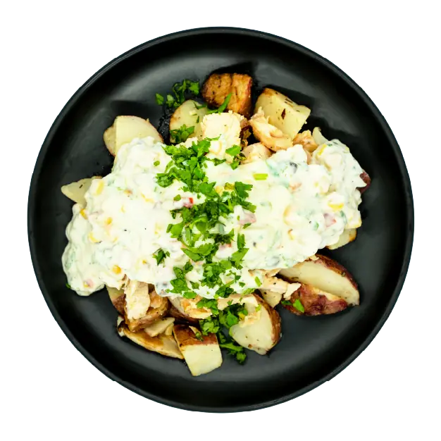 Chicken with creamy street corn sauce over roasted red potatoes on a black plate.