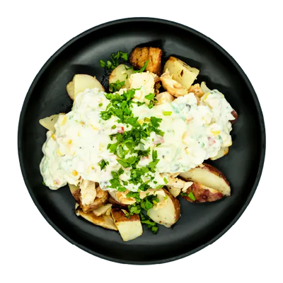 Chicken with creamy street corn sauce over roasted red potatoes on a black plate.