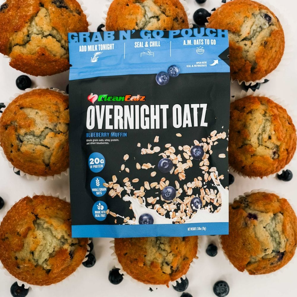 Clean Eatz Overnight Oatz Blueberry Muffin flavor pouch placed among blueberry muffins – grab-and-go breakfast with 20g of protein and real blueberries