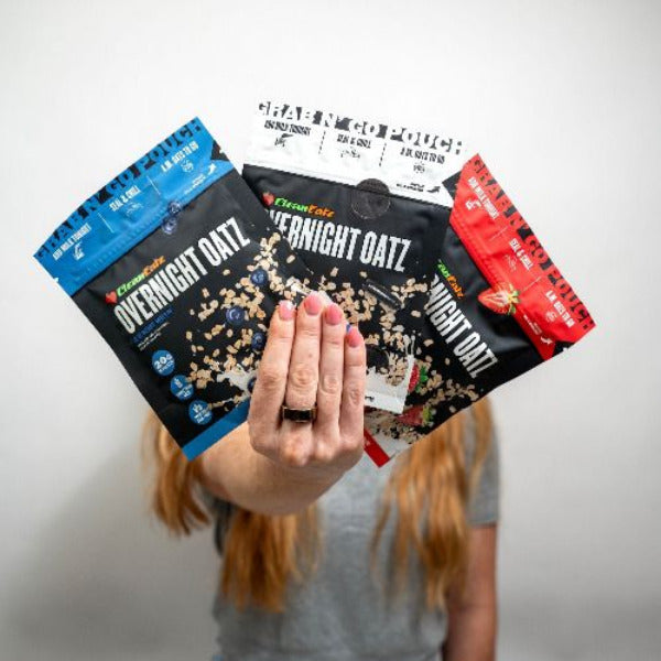 Person holding three packages of Clean Eatz 'Overnight Oats' with a plain background