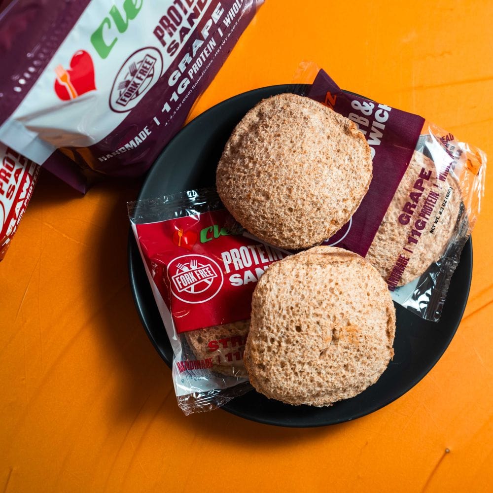 Two protein sandwiches on a black plate with packaging on an orange background